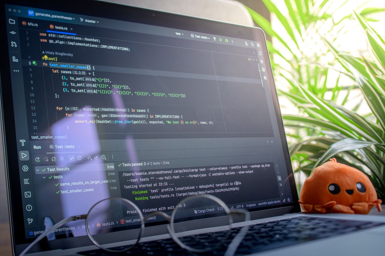 Home Open laptop displaying code next to a plush toy, set in a bright room with plants.