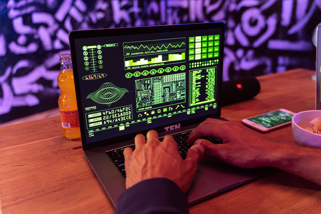 Services A person typing on a laptop displaying green code with an orange bottle and smartphone nearby.